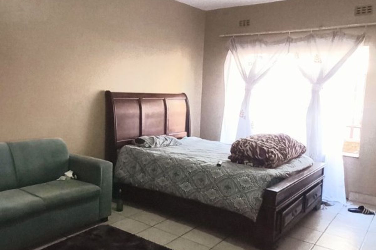 A bedroom featuring tiled flooring and a window with a curtain rail, providing a functional living space.