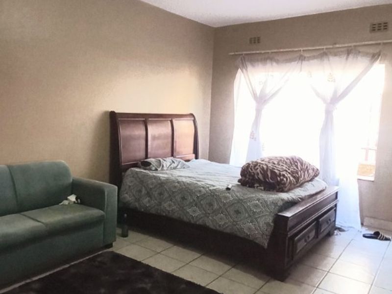 A bedroom featuring tiled flooring and a window with a curtain rail, providing a functional living space.