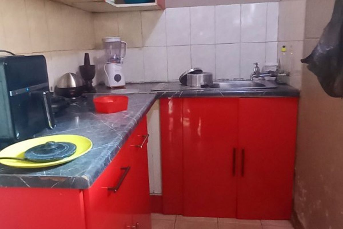 A compact kitchen featuring red cabinetry, a laminate countertop, and a stainless steel sink with tiled backsplash and flooring.