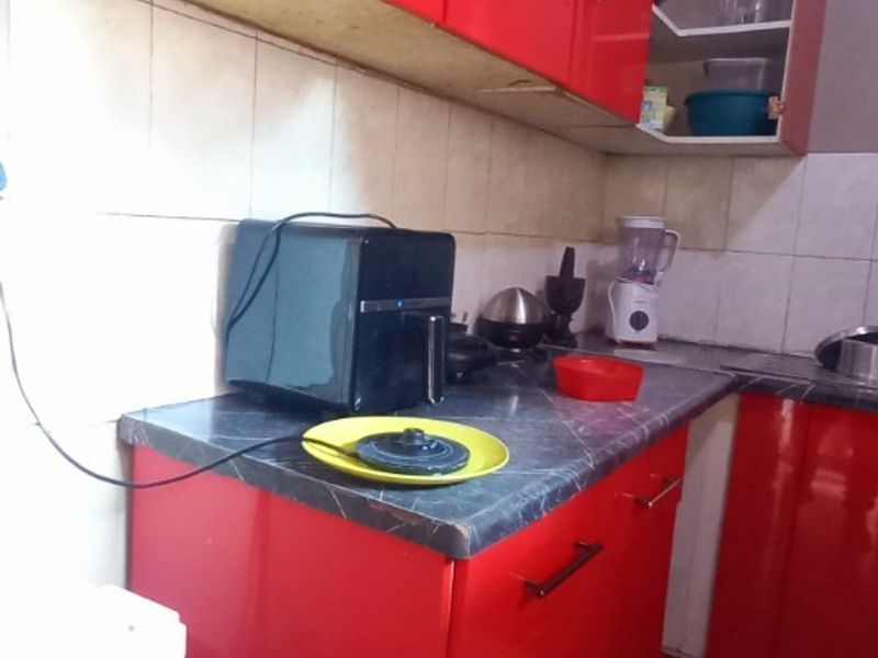 A compact kitchen featuring red cabinetry, tiled backsplash, and laminate countertops, requiring cosmetic updates to improve the overall aesthetic and finish.