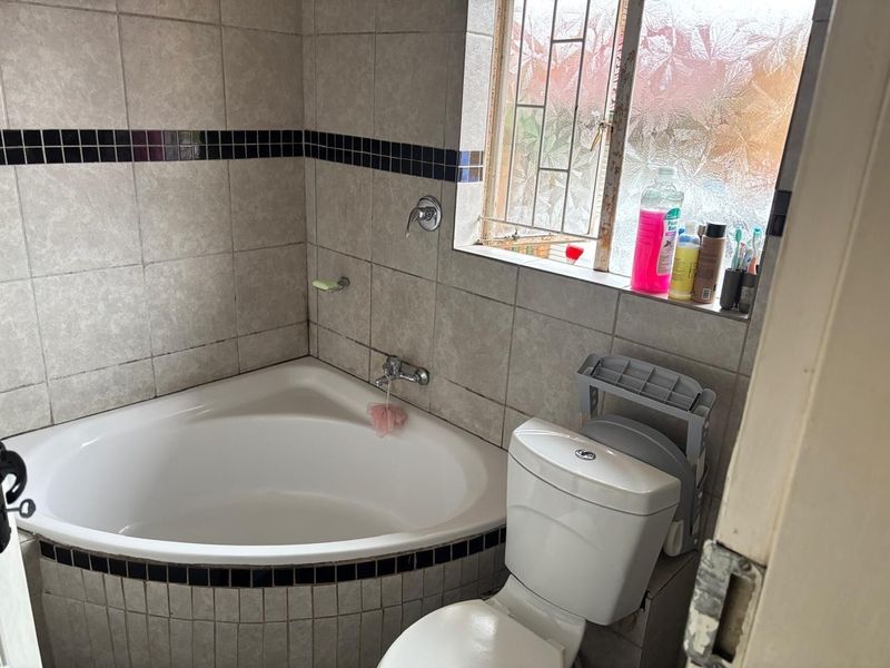 A compact bathroom featuring a corner bathtub, toilet, and tiled walls with decorative accents, requiring some maintenance and updates.