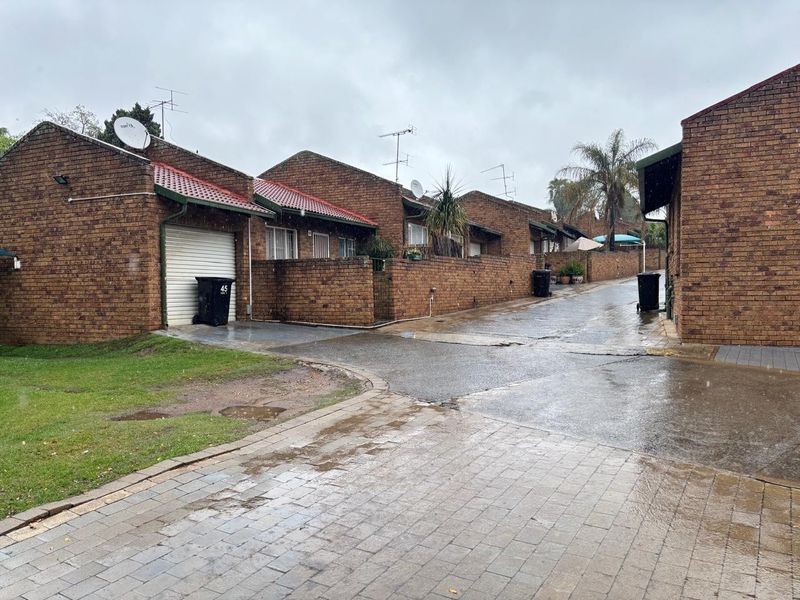 Exterior view of a face brick townhouse complex featuring paved driveways, roller garage doors, and boundary walls under an overcast sky.