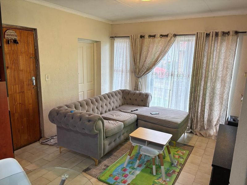 A living room area featuring tiled flooring and a sliding glass door providing natural light, with potential for cosmetic updates to finishes.