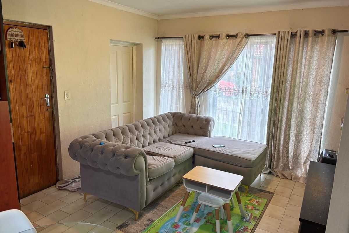 A living room area featuring tiled flooring and a sliding glass door providing natural light, with potential for cosmetic updates to finishes.