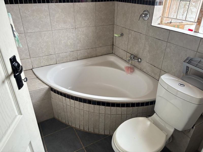A compact bathroom featuring a corner bathtub, tiled walls with decorative accents, and a standard toilet.
