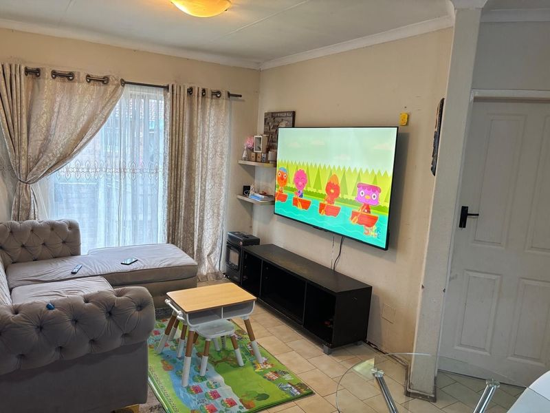 A functional living room featuring tiled flooring, a sliding glass door for natural light, and a wall-mounted television setup.