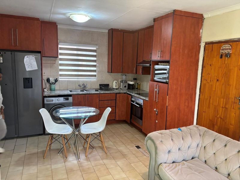 Functional kitchen featuring wood-finish cabinetry, tiled backsplash, built-in oven and hob, and integrated laundry plumbing, offering a practical layout for daily use.