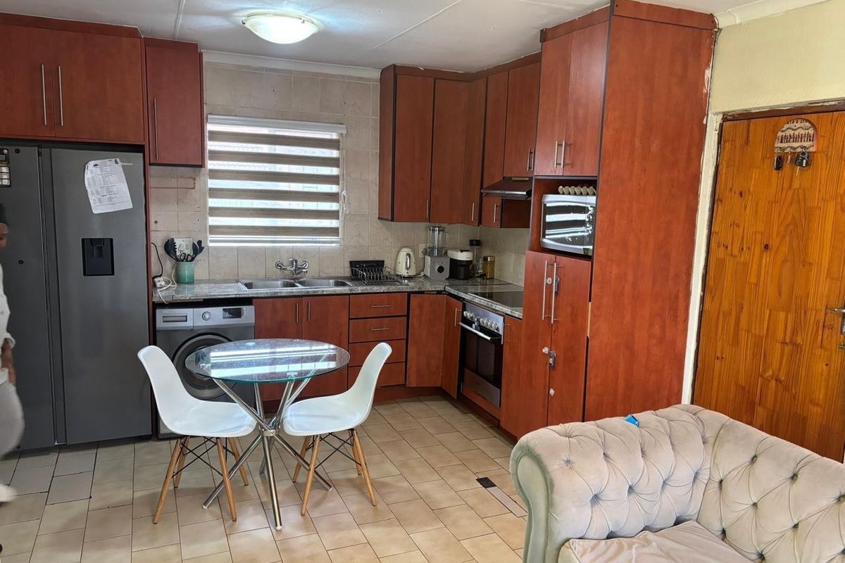 Functional kitchen featuring wood-finish cabinetry, tiled backsplash, built-in oven and hob, and integrated laundry plumbing, offering a practical layout for daily use.