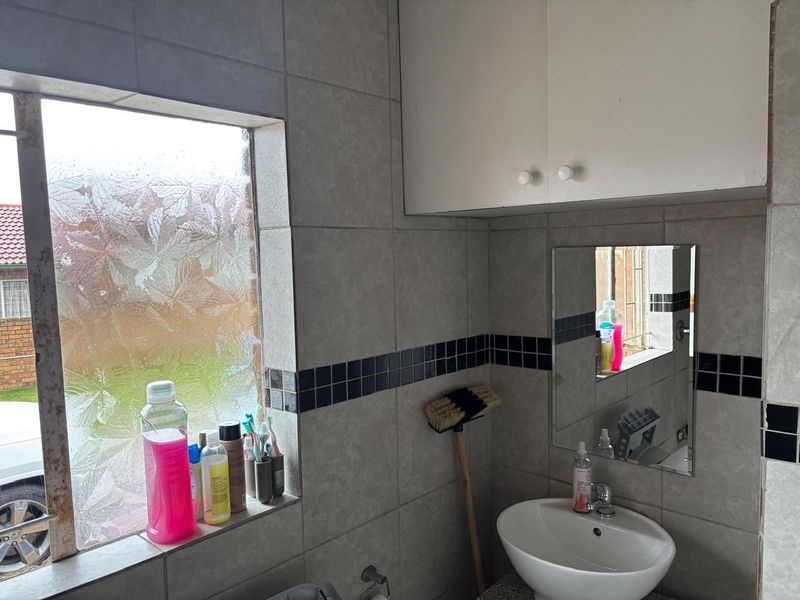 A functional bathroom featuring tiled walls, a wall-mounted vanity cabinet, a ceramic basin, and an obscured glass window.