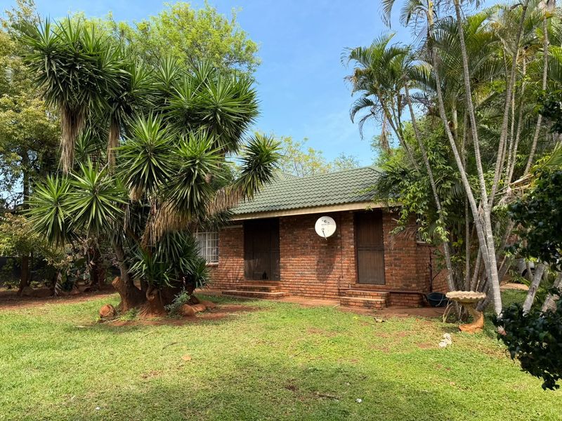 A rear view of a face brick house featuring a tiled roof, satellite dish, and established garden surroundings.