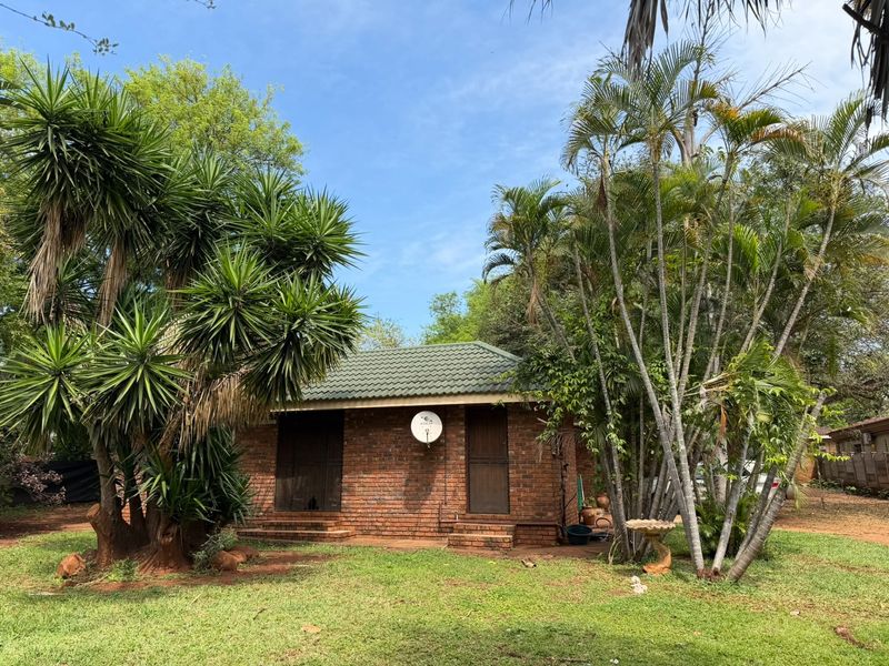 A detached face brick structure featuring a tiled roof, set within a mature garden with established trees and shrubs.