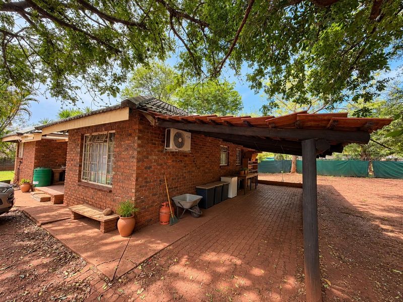 Rear view of a brick house featuring a covered patio area with timber supports and paved flooring, set within a spacious garden.