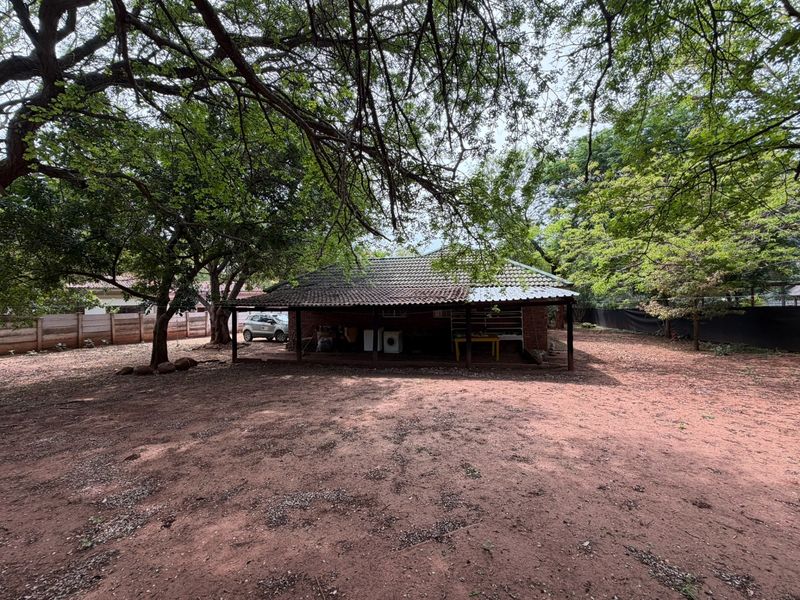 Rear view of the house featuring a covered patio area, brick exterior, and a large, unpaved garden space shaded by mature trees.