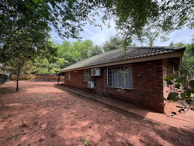 Rear view of a face brick house featuring a tiled roof, security bars on windows, and installed split-unit air conditioning units.