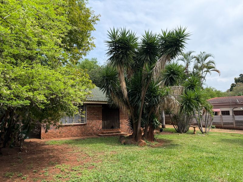 Front view of a face brick house featuring a tiled roof, security window bars, and a spacious established garden.