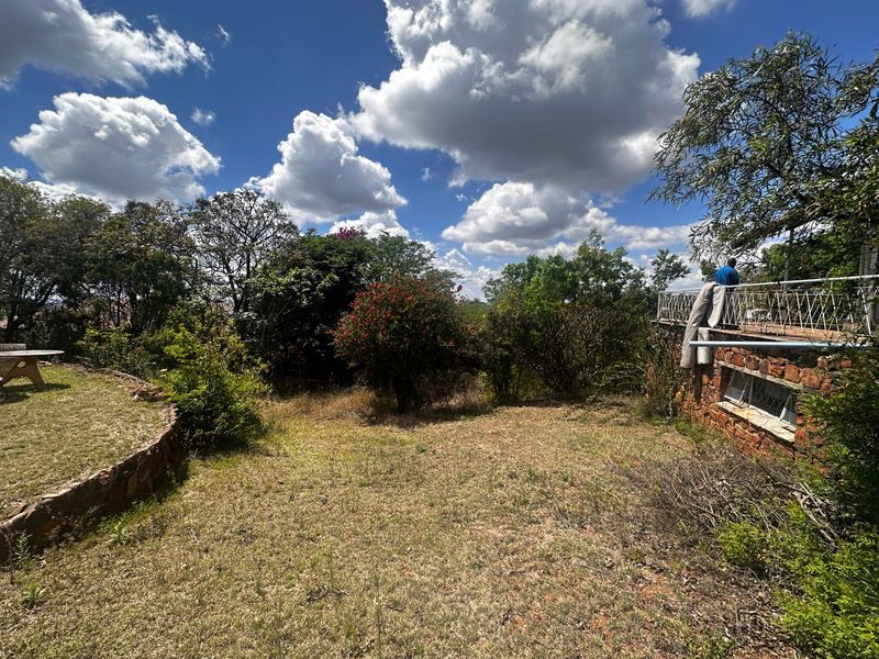 A rear garden area featuring a stone retaining wall, a raised patio with metal railings, and established trees and shrubs.