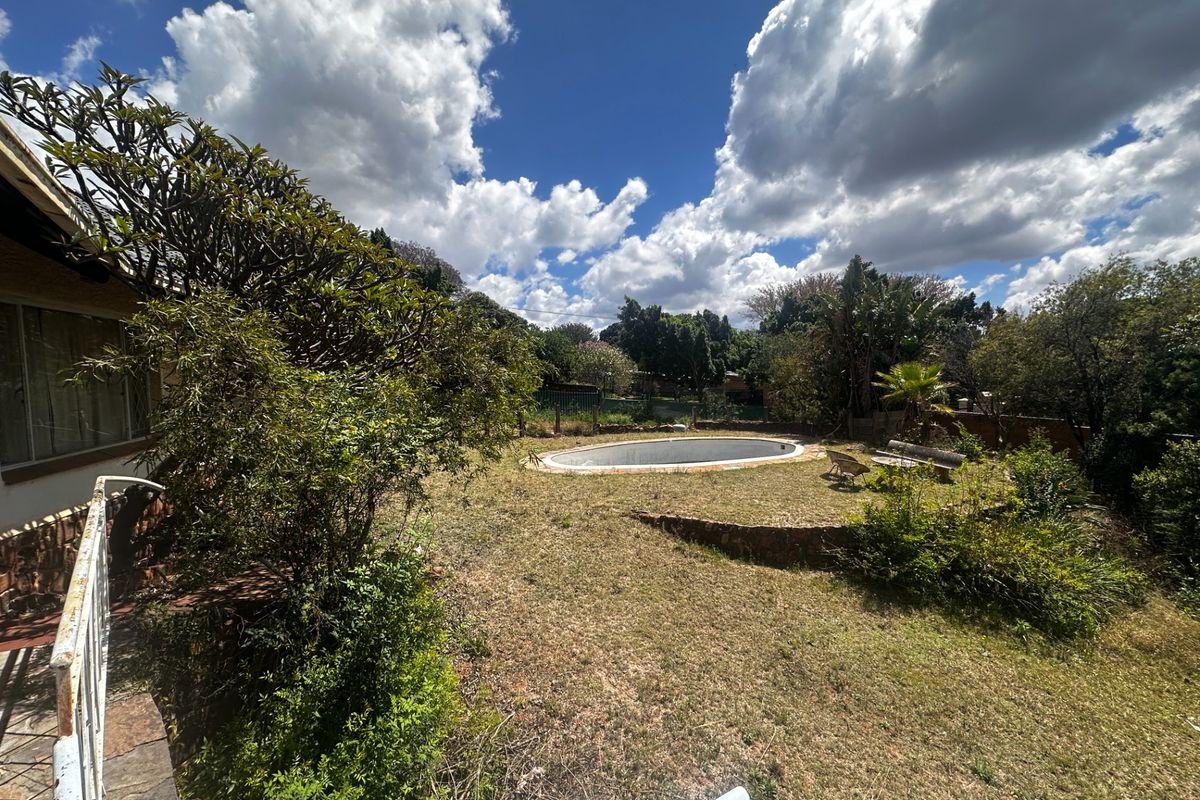 Outdoor backyard area featuring an empty swimming pool, stone retaining wall, and established garden space with potential for landscaping.