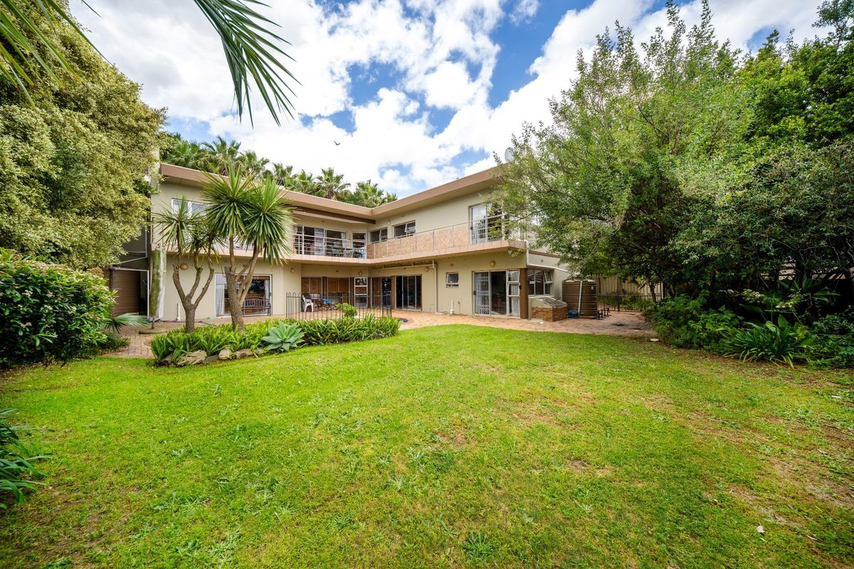 Spacious rear exterior view of a two-story house featuring a large lawn, paved patio area, and upper-level balcony with security railings.