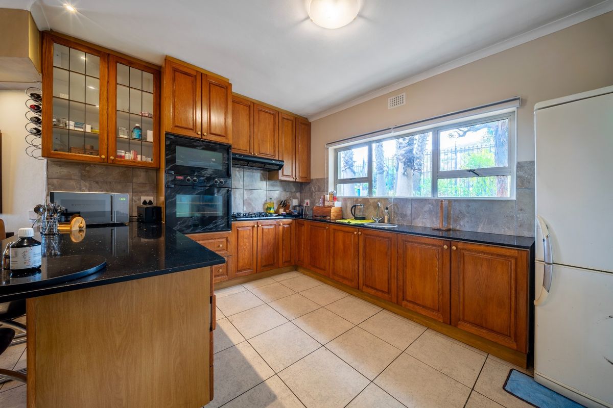 A functional kitchen featuring warm wooden cabinetry, black granite countertops, built-in appliances, and tiled flooring with a large window providing natural light.