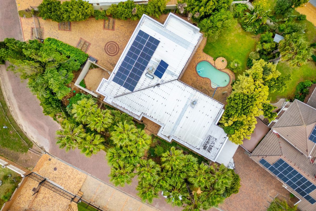 Aerial view of the property showcasing the metal roof with solar panels, a swimming pool, landscaped garden, and paved driveway.