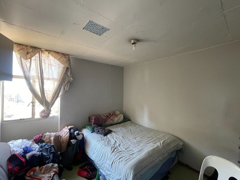A bedroom featuring a tiled ceiling with a ventilation grille, requiring cosmetic updates and repairs to the ceiling and wall finishes.