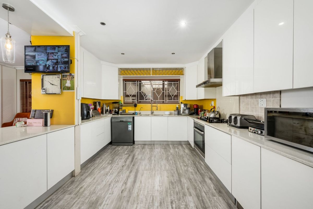 Modern kitchen featuring white gloss cabinetry, stone countertops, built-in oven, gas hob, and stainless steel extractor fan with ample workspace.