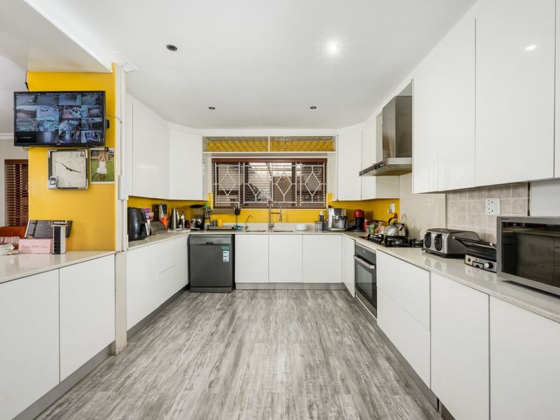 Modern kitchen featuring white gloss cabinetry, stone countertops, built-in oven, gas hob, and stainless steel extractor fan with ample workspace.