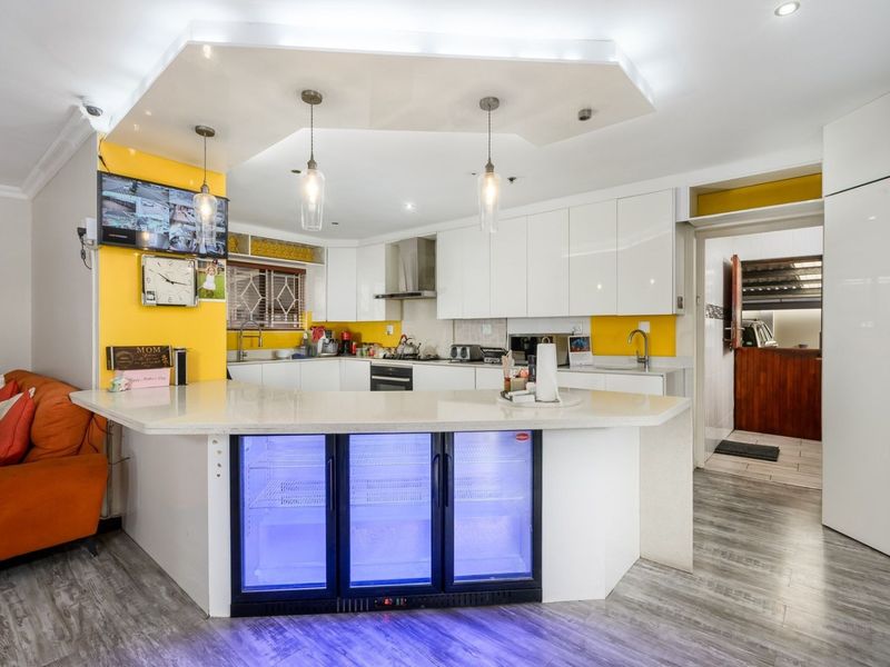 Modern kitchen featuring white high-gloss cabinetry, stone countertops, integrated beverage cooler, and a distinctive drop ceiling with recessed and pendant lighting.