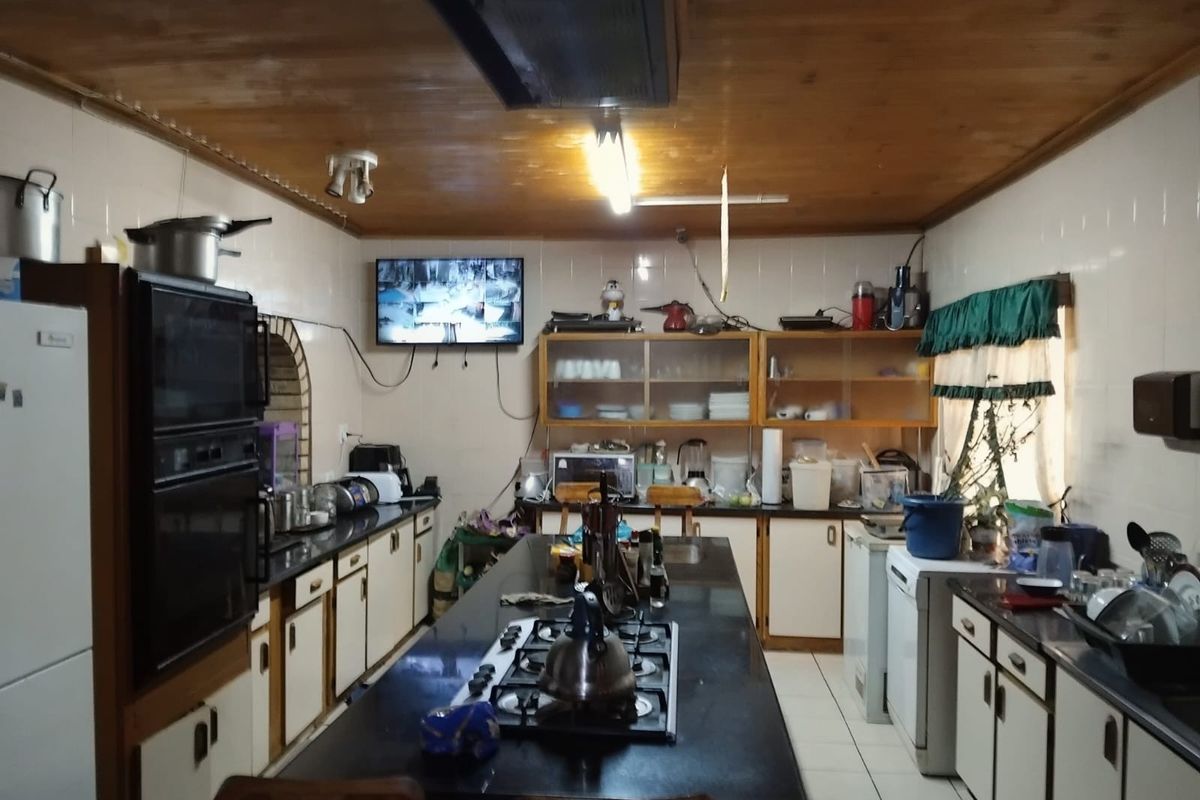 Spacious kitchen featuring a central island with a gas hob, built-in oven, ample cabinetry, and granite countertops under a timber-clad ceiling.