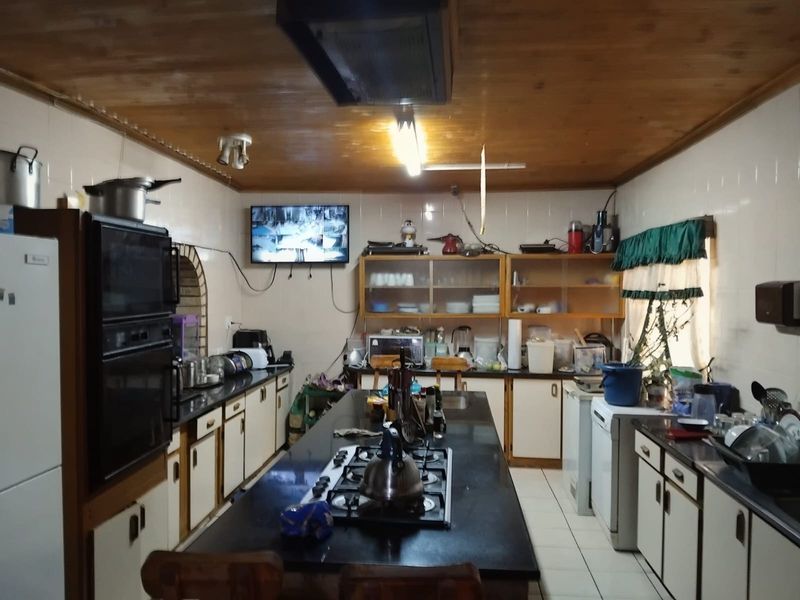 Spacious kitchen featuring a central island with a gas hob, built-in oven, ample cabinetry, and granite countertops under a timber-clad ceiling.