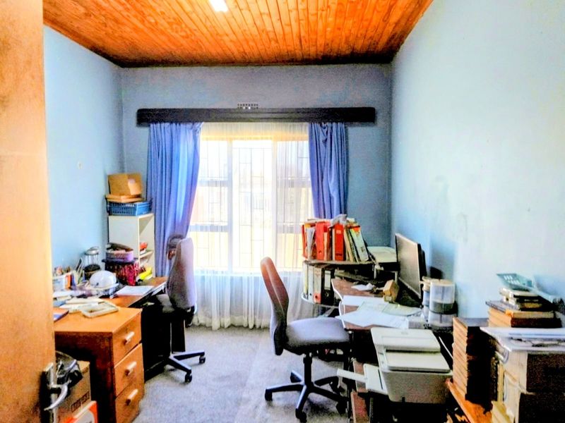 A functional home office space featuring a wooden tongue and groove ceiling, carpeted flooring, and security burglar bars on the window.