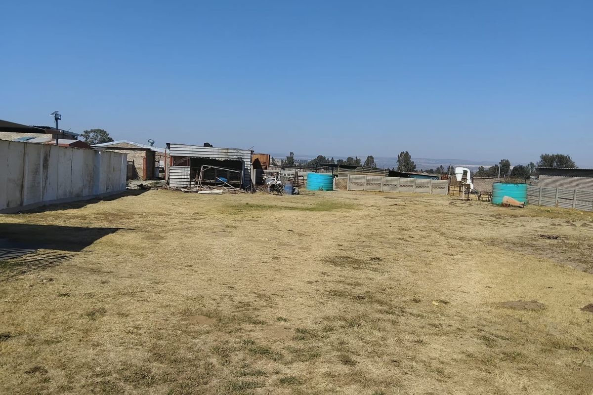 A large, open rear yard area featuring a precast concrete boundary wall, water storage tanks, and a dilapidated outbuilding structure.