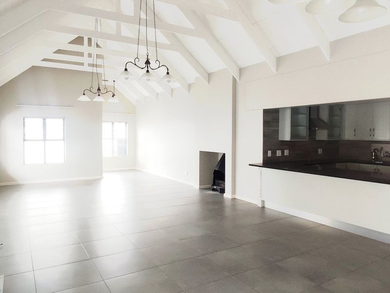 Spacious open-plan living area featuring vaulted ceilings with exposed rafters, tiled flooring, a built-in fireplace, and a modern kitchen with granite countertops.