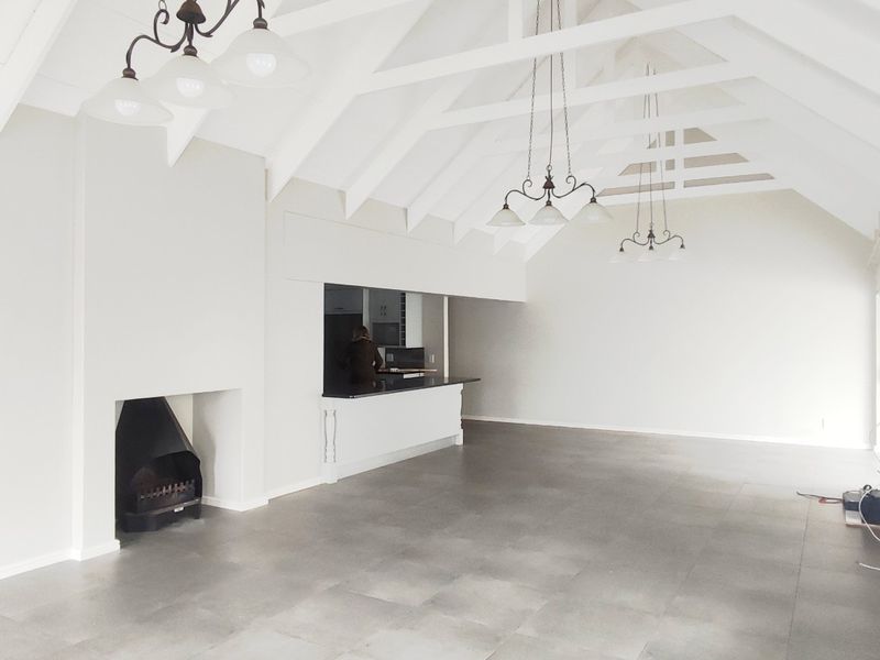 Spacious open-plan living area featuring a vaulted ceiling with exposed rafters, tiled flooring, a built-in fireplace, and a breakfast bar.
