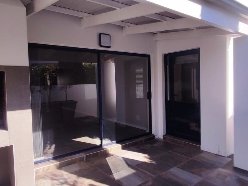 A covered outdoor patio featuring a built-in braai, tiled flooring, and direct access to the interior through sliding glass doors.