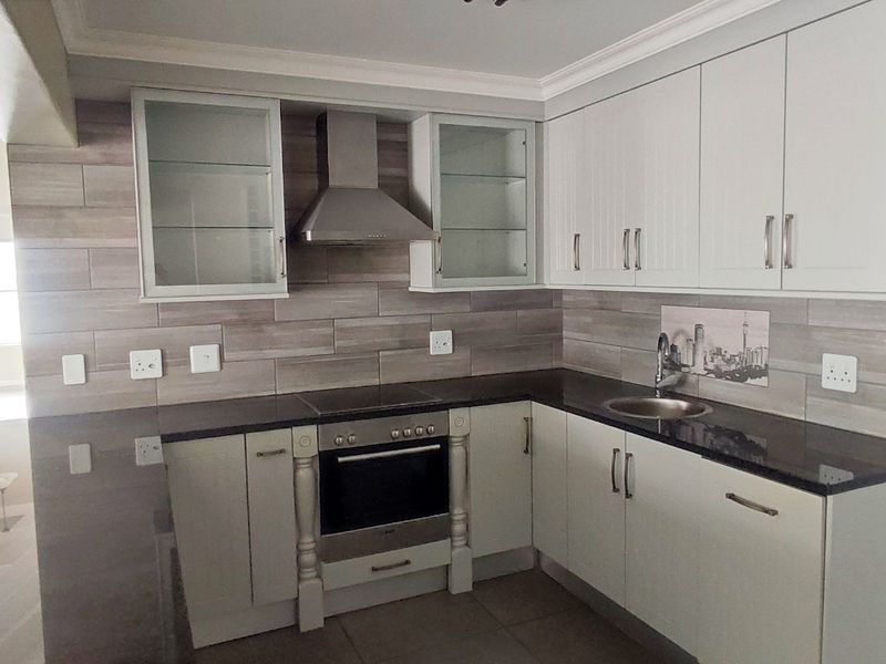 A modern, well-maintained kitchen featuring white cabinetry, dark stone countertops, a built-in oven with extractor fan, and a tiled backsplash.