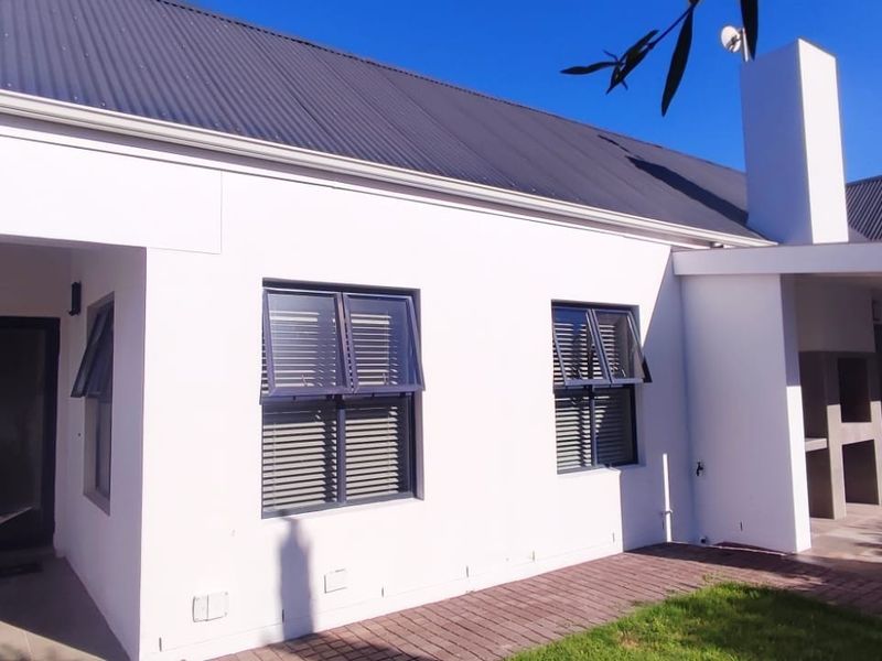 Rear elevation of a modern home featuring a corrugated metal roof, paved patio area, and a built-in outdoor braai facility.