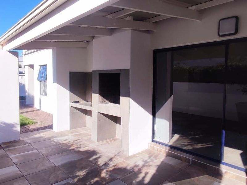 A covered patio area featuring a built-in braai, tiled flooring, and large sliding glass doors leading into the home.