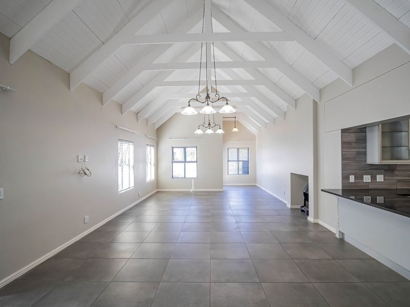 Spacious open-plan living area featuring a high vaulted ceiling with exposed trusses, tiled flooring, a built-in fireplace, and a modern kitchen with granite countertops.
