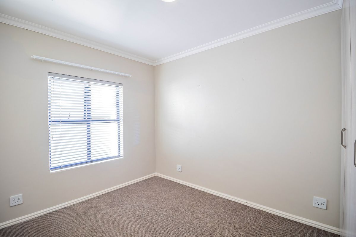 A clean, empty bedroom featuring neutral carpeting, built-in wardrobe storage, and venetian blinds, providing a versatile space ready for personalization.
