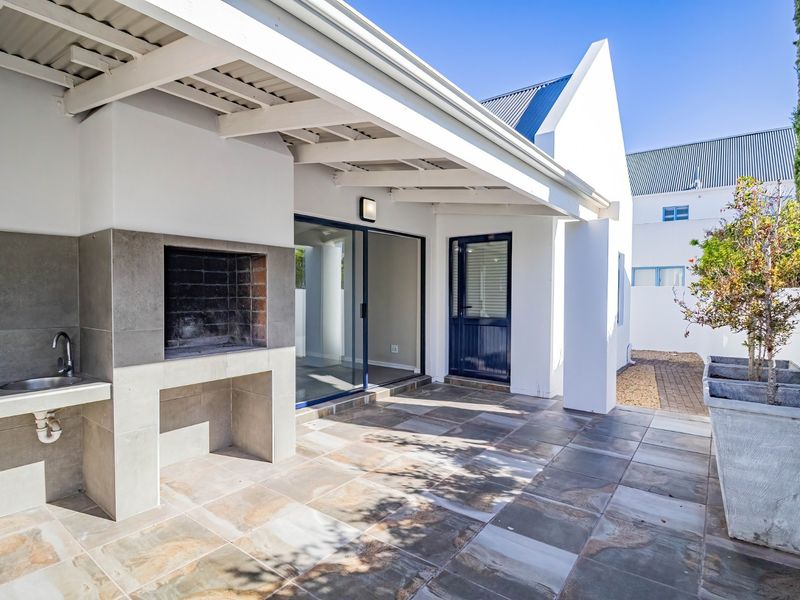 A well-maintained covered patio featuring a built-in braai, outdoor sink, and tiled flooring, providing a seamless transition to the interior living space.