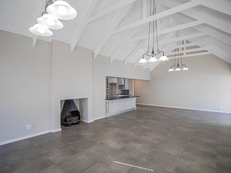 Spacious open-plan living area featuring a vaulted ceiling with exposed beams, tiled flooring, a built-in fireplace, and a breakfast bar connecting to the kitchen.
