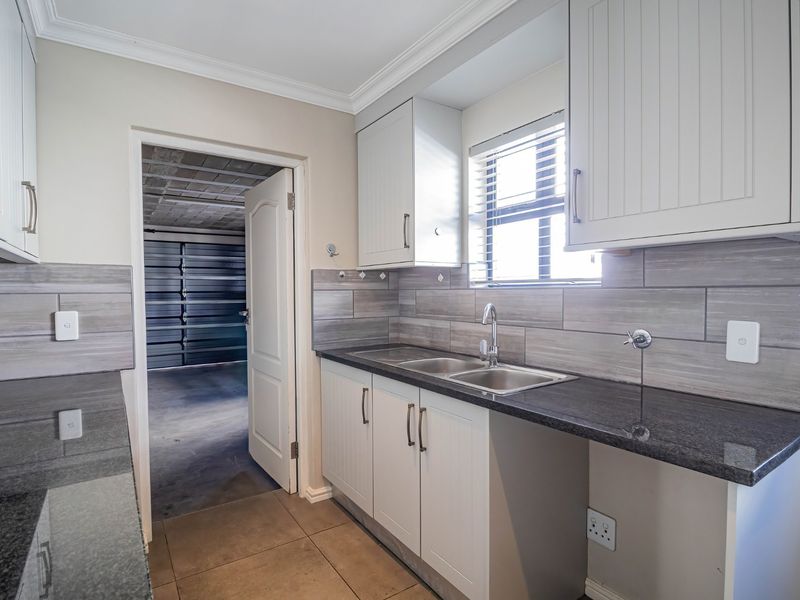 A clean and functional scullery featuring granite countertops, double basin sink, shaker style cabinetry, and modern tiled backsplash with direct access to the garage.