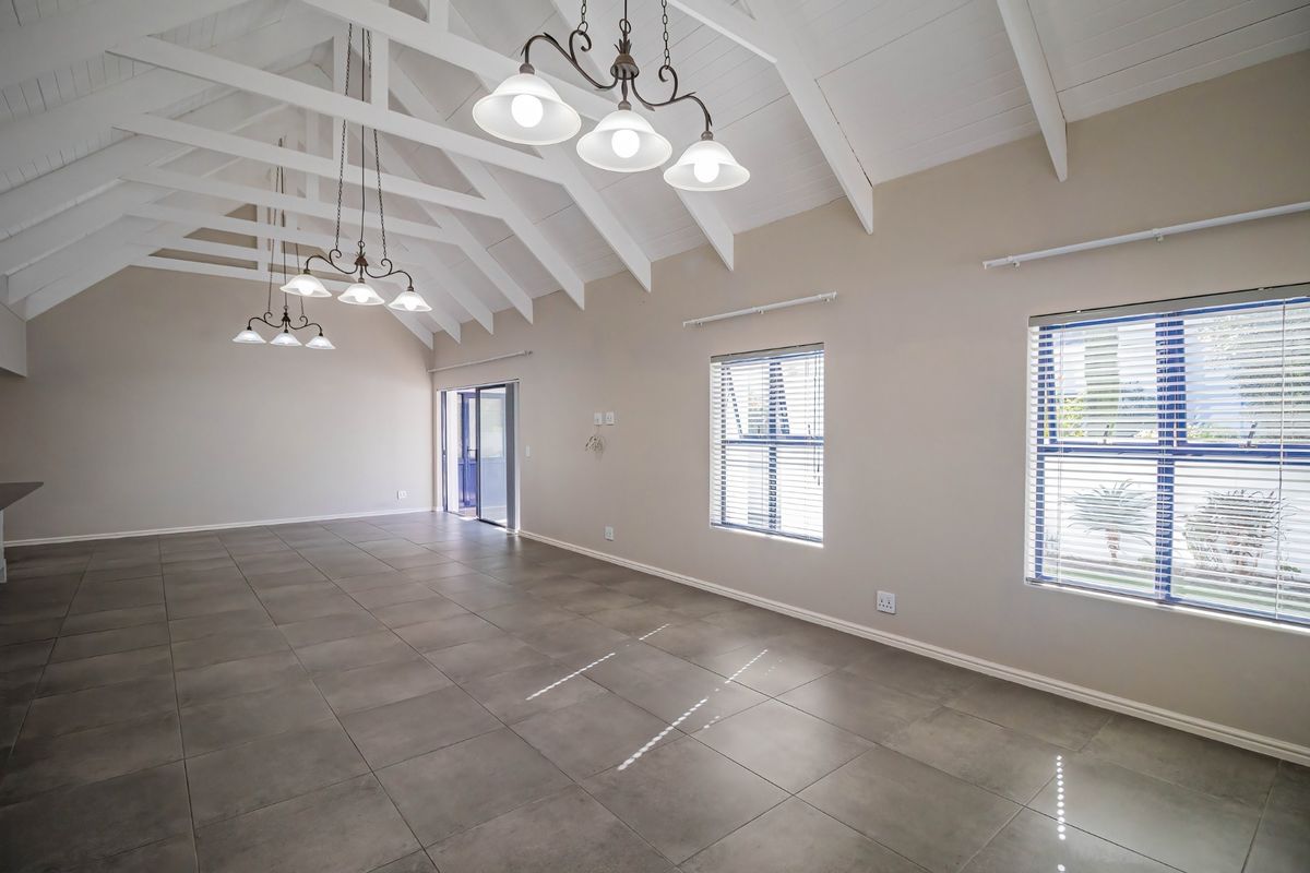 Spacious living area featuring high vaulted ceilings with exposed trusses, large tiled floors, and abundant natural light through sliding doors and windows.