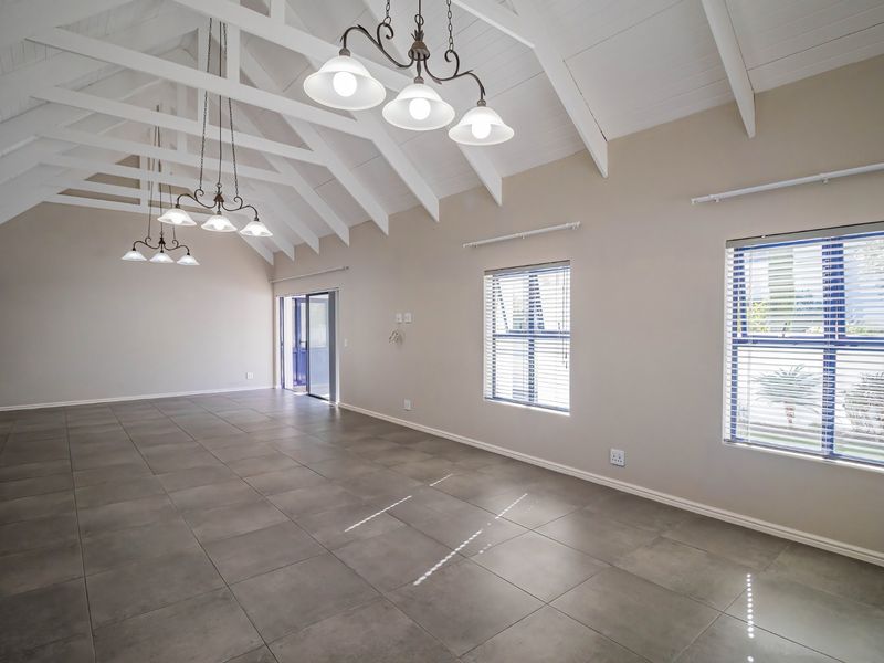 Spacious living area featuring high vaulted ceilings with exposed trusses, large tiled floors, and abundant natural light through sliding doors and windows.
