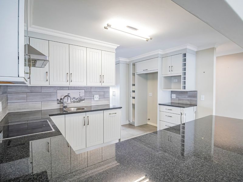 Modern kitchen featuring white cabinetry, dark granite countertops, integrated hob, stainless steel extractor fan, and a tiled backsplash.