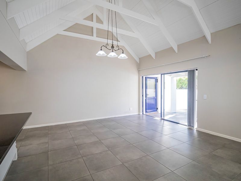 Spacious open-plan living area featuring high vaulted ceilings with exposed trusses, modern tiled flooring, and direct access to an outdoor patio through sliding doors.