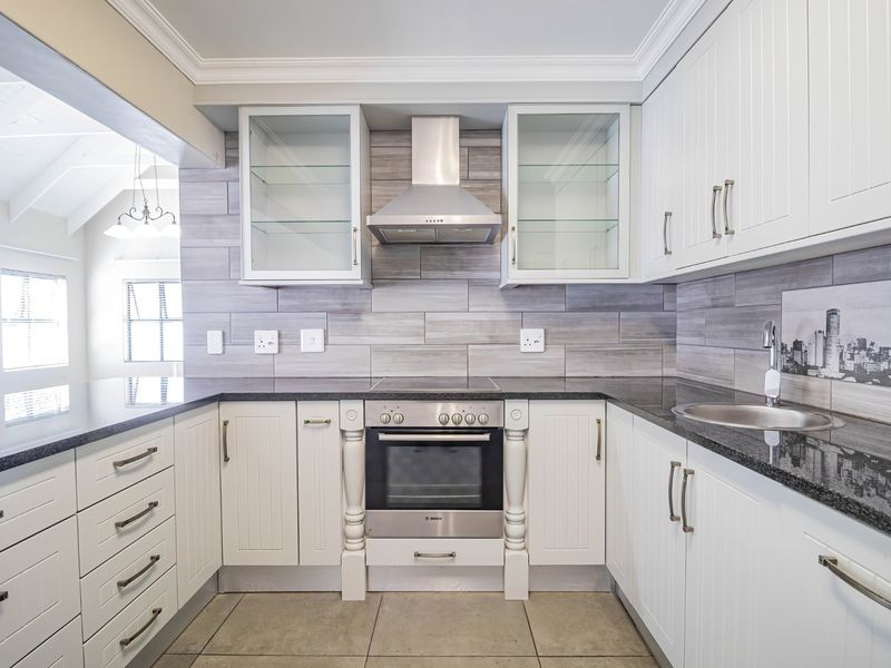 Modern kitchen featuring white cabinetry, granite countertops, built-in oven, stainless steel extractor fan, and stylish tiled backsplash with a view into the living area.