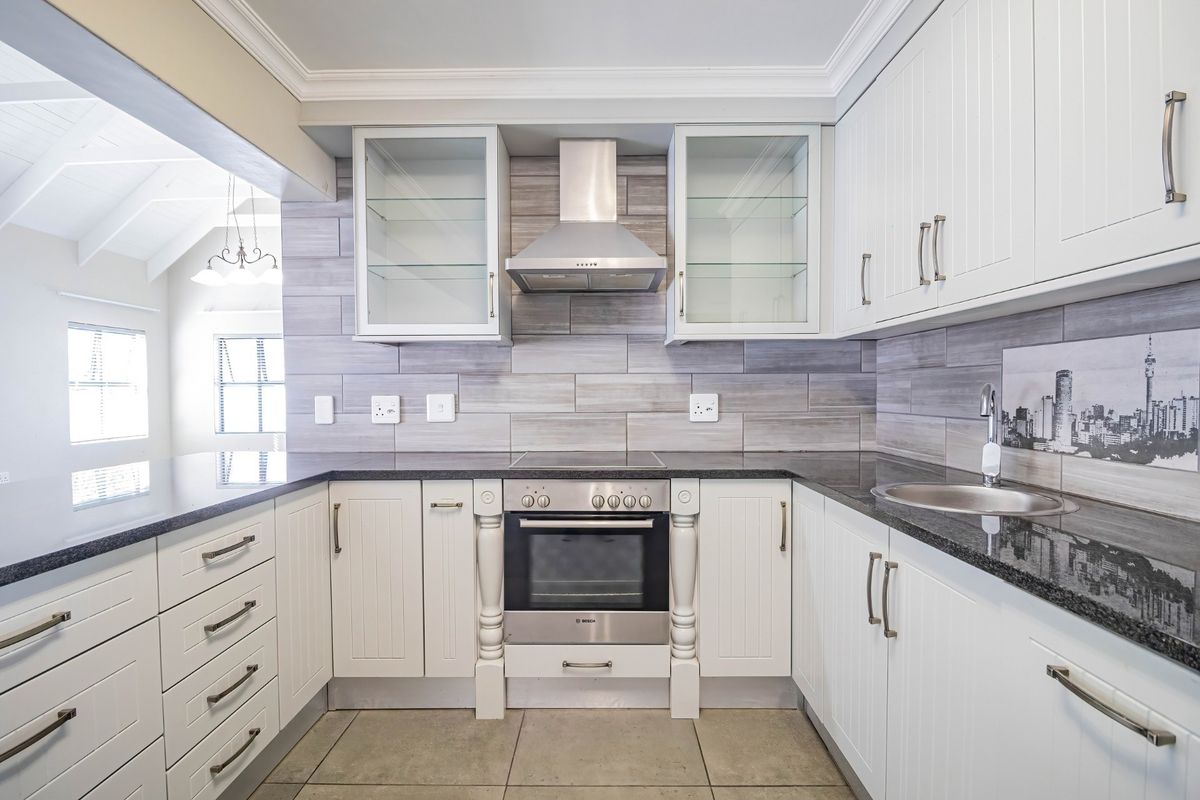 Modern kitchen featuring white cabinetry, granite countertops, built-in oven, stainless steel extractor fan, and stylish tiled backsplash with a view into the living area.