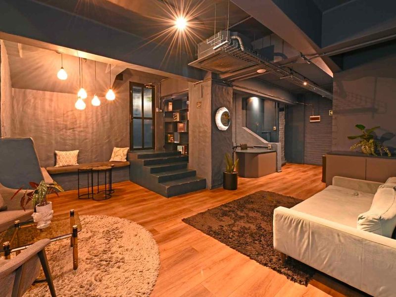 A stylish, modern living area featuring exposed industrial ceiling ducting, warm hardwood flooring, and unique built-in bench seating with ambient pendant lighting.